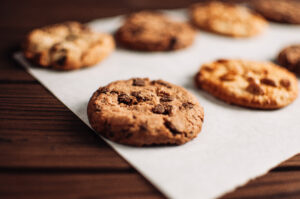 chocolate covered cookies lay on a parchment paper in a row. gluten free cookies on a wooden table out of the oven. selective focus