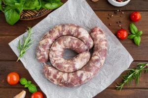 raw sausages on paper with spices and fresh herbs on a dark wooden background. top view, copy space.