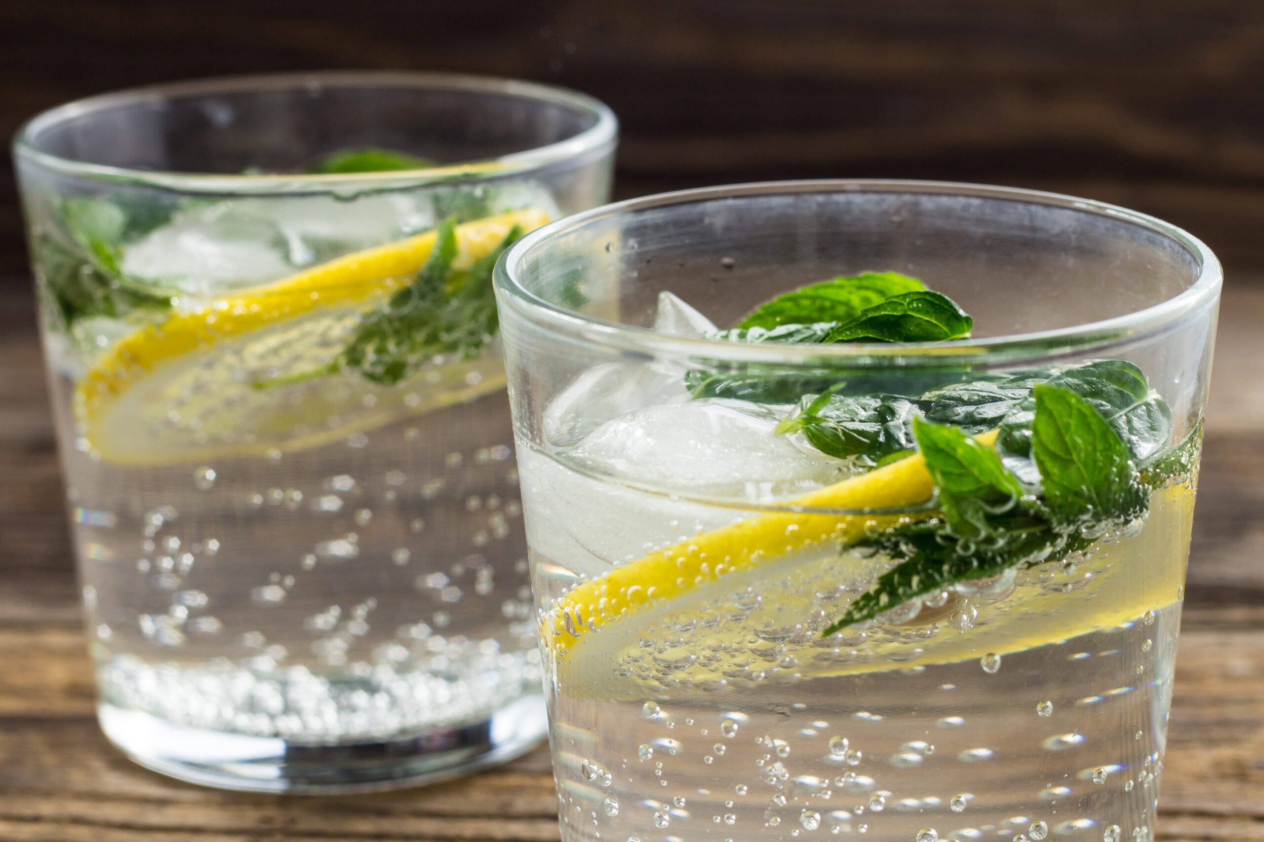 two glasses of lemonade with lemon, mint and ice cubes on wooden background. summer drink